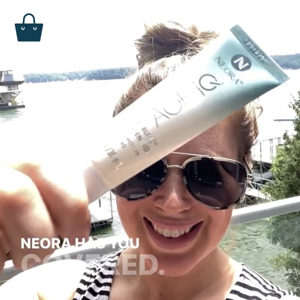 Woman smiling and holding Neora’s Invisi-Bloc SPF40 Sunscreen Gel.